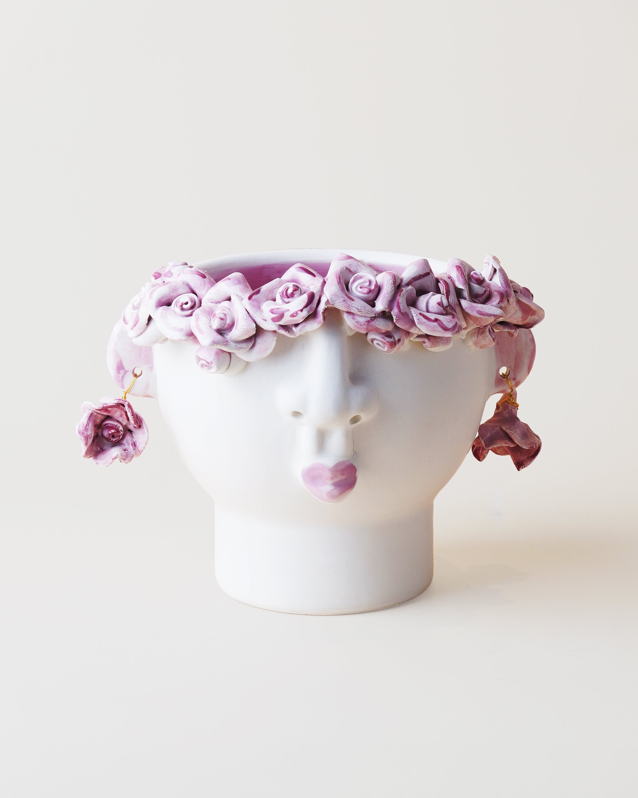 White ceramic head with a pink floral crown on a light beige background