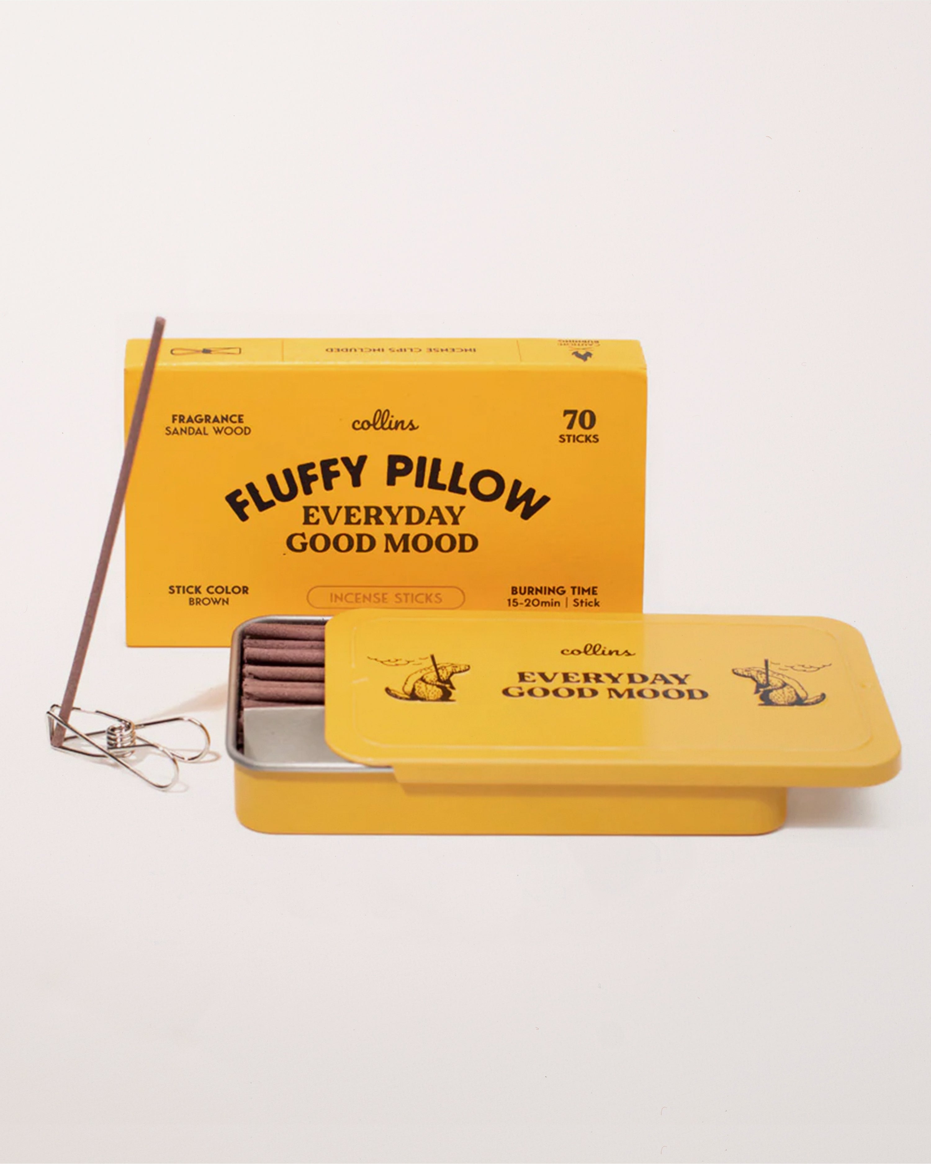 A yellow tin of Collins Co. Fluffy Pillow incense with incense sticks displayed in front of it.