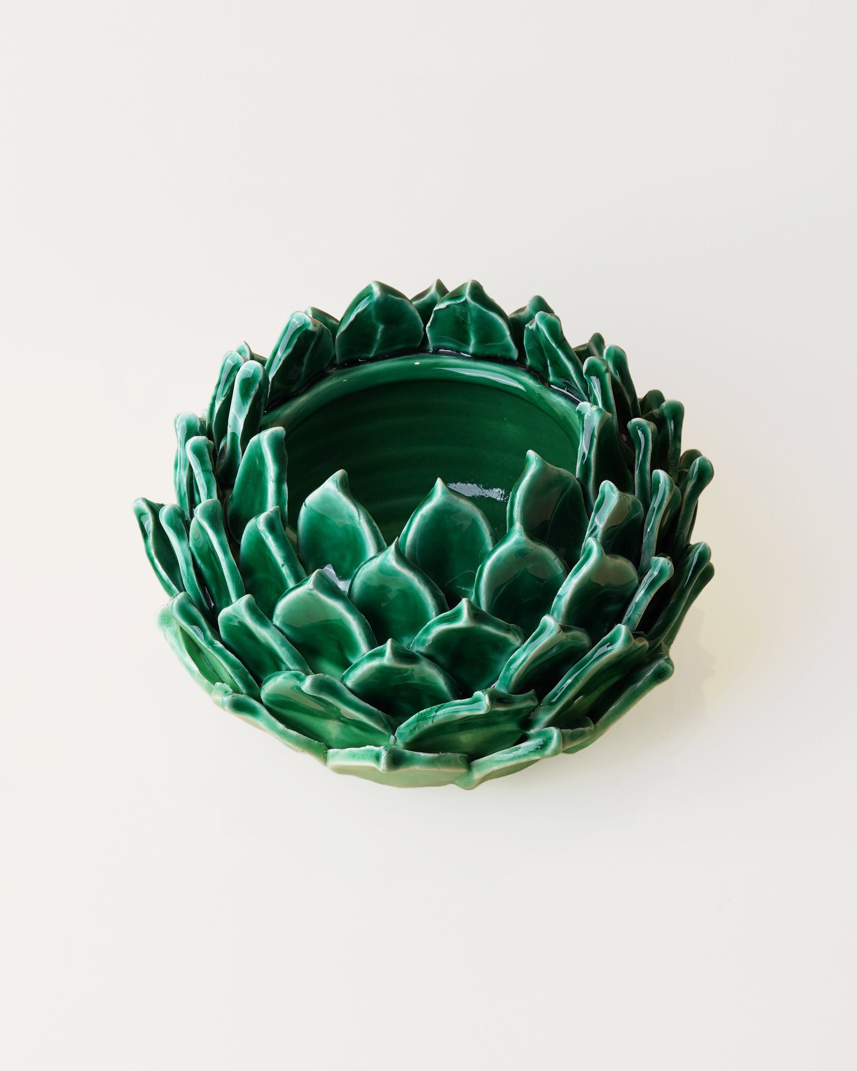 A green ceramic dish shaped like a lotus flower, photographed from a top-down view on a plain white background.