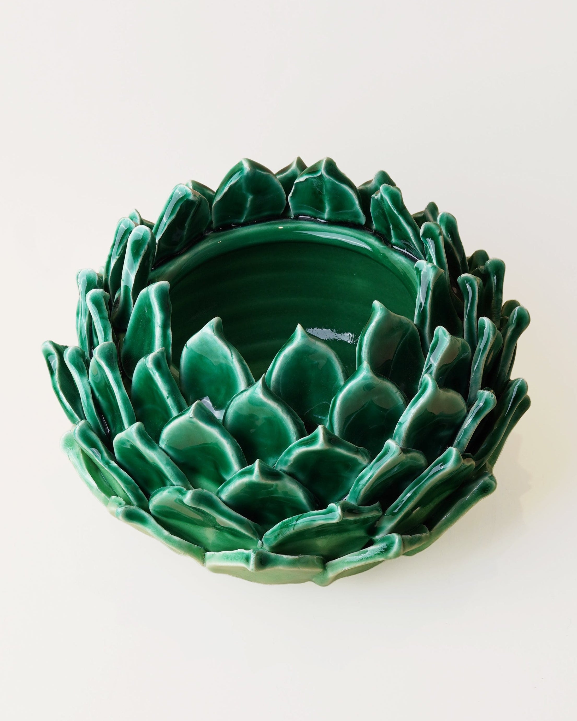 A green ceramic dish shaped like a lotus flower, photographed from a top-down view on a plain white background.