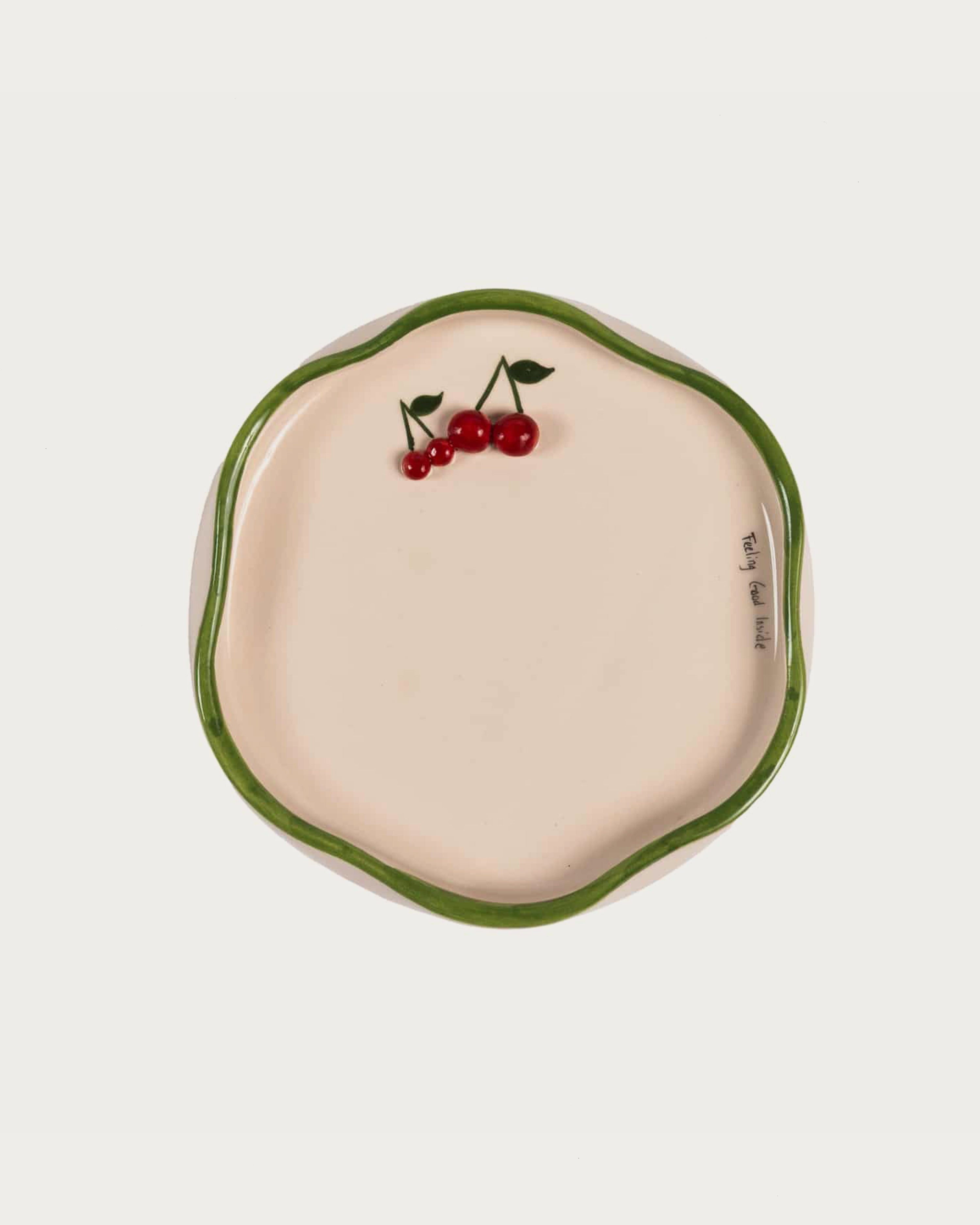 Ceramic dish with green rim and cherry design on a white background
