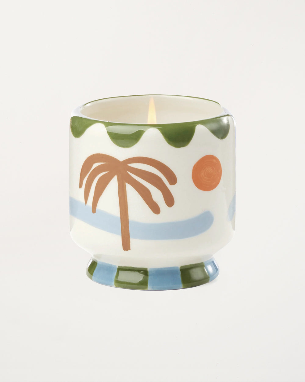 Candle in a decorative container with palm tree and sun design on a white background