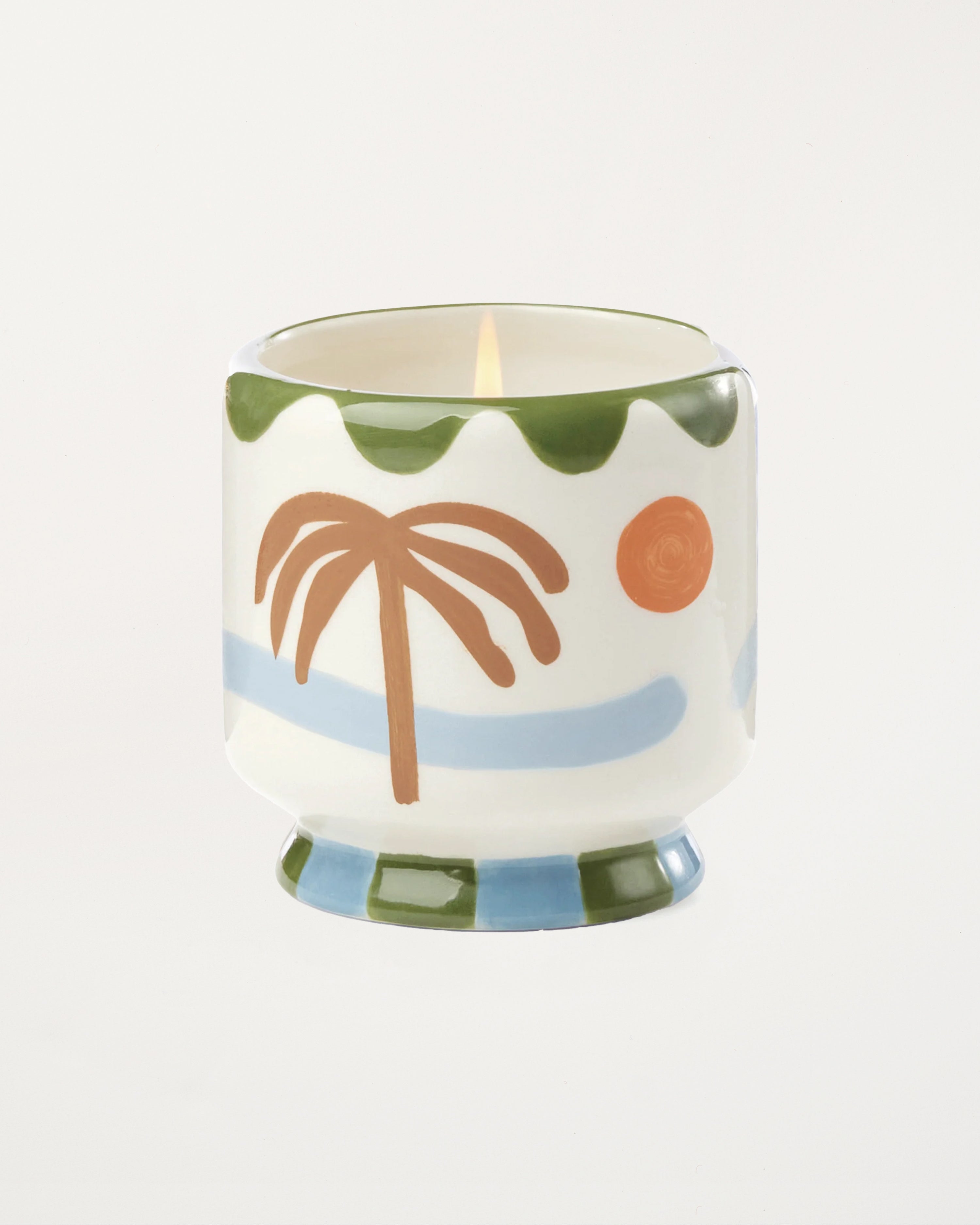 Candle in a decorative container with palm tree and sun design on a white background