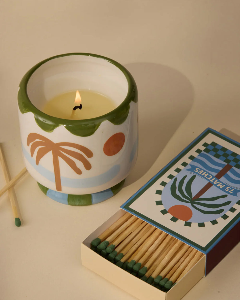 Candle in a decorative container with palm tree and sun design on a white background