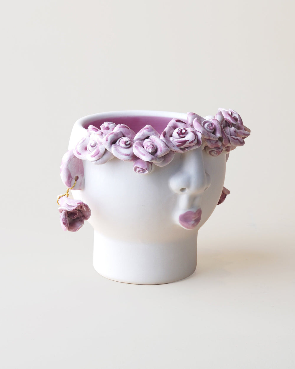 White ceramic head with a pink floral crown on a light beige background