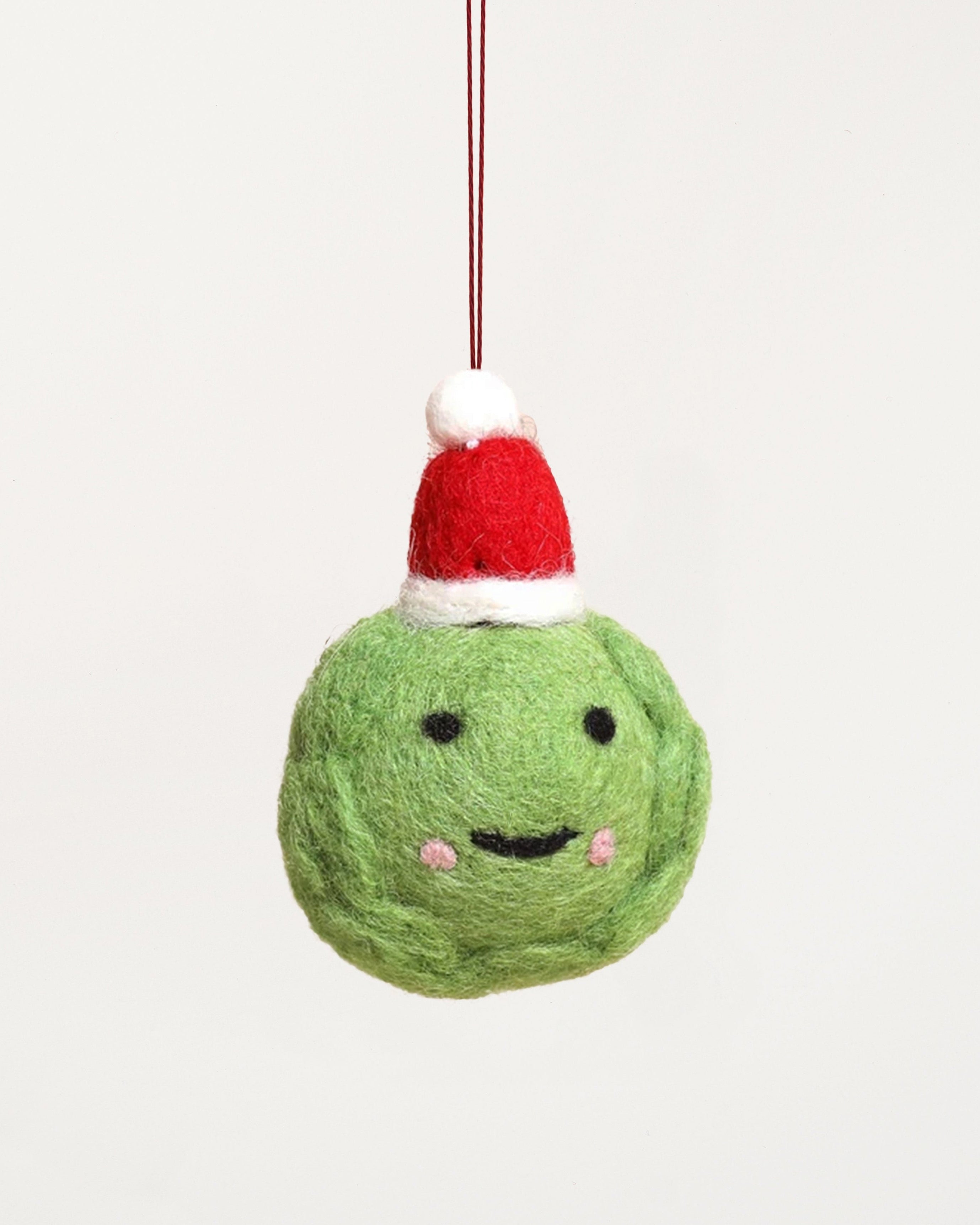 Green textured Christmas ball with a face and red and white hat on a beige background