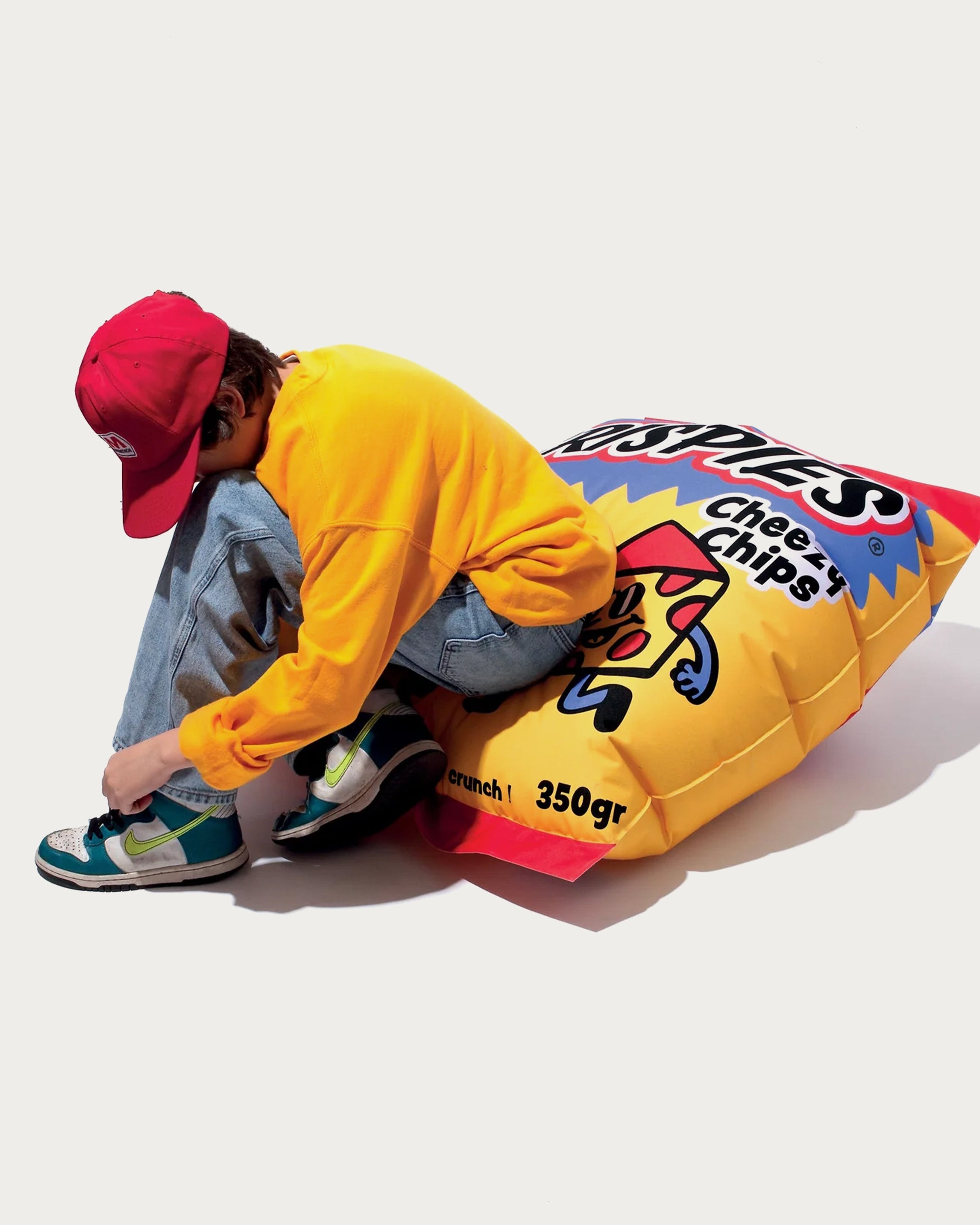 Person sitting on a large colorful bag of chips with a plain background