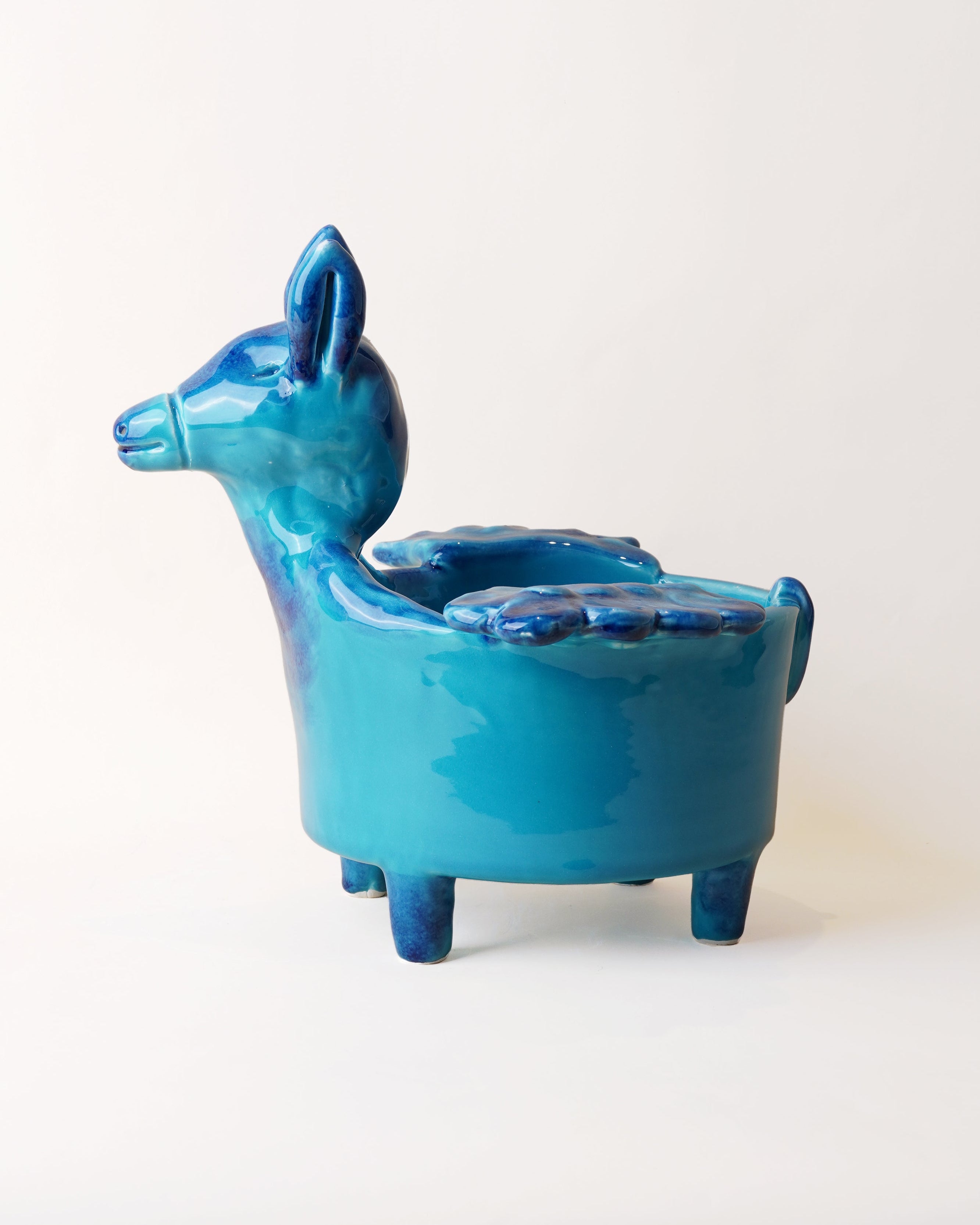 A ceramic deer-shaped stool in a glossy turquoise blue glaze, photographed against a plain off-white background.
