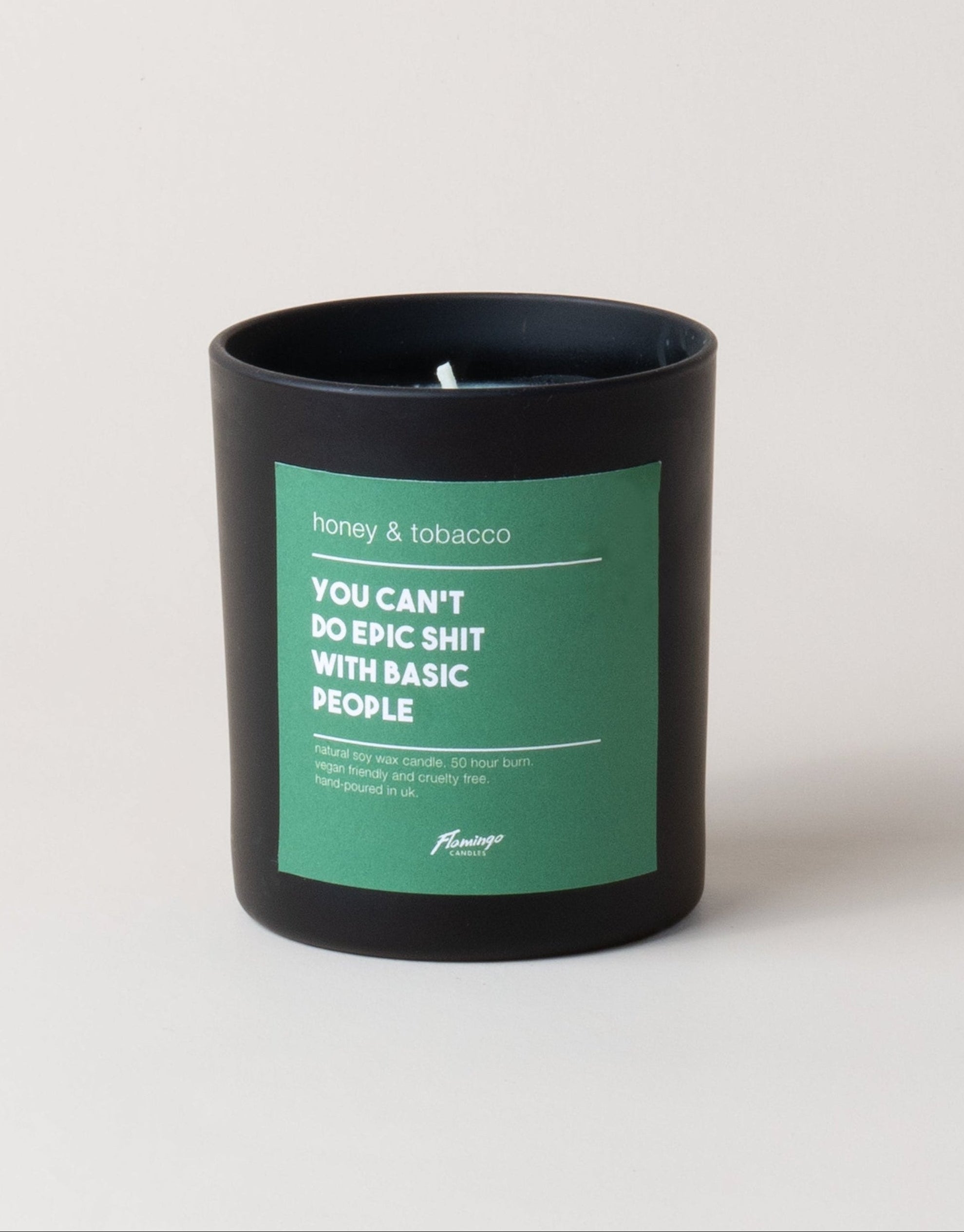 A black jar candle with a green label that reads 'Honey & Tobacco. You can't please all the people all the time.'