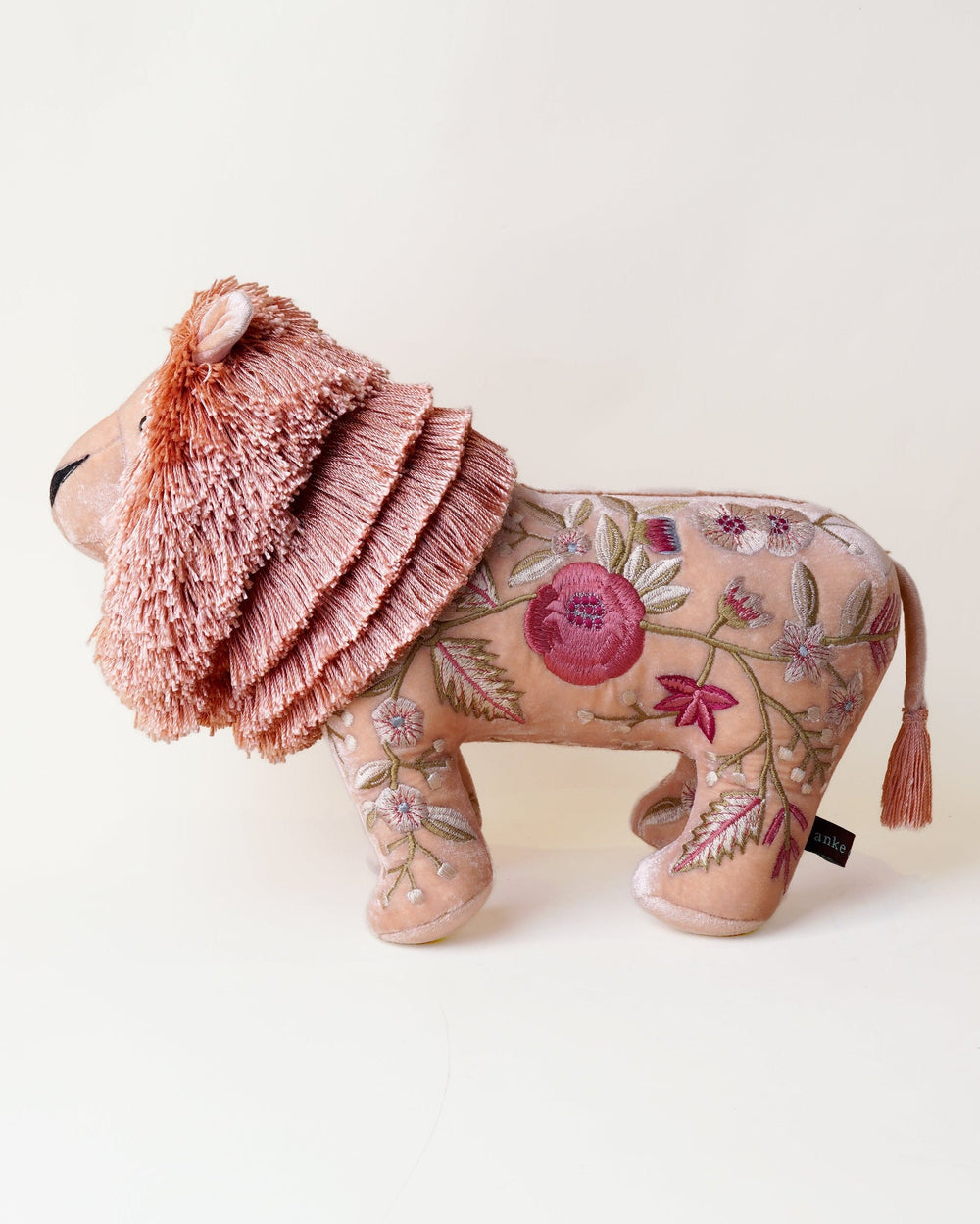 A handmade plush lion toy with a shaggy pink mane and a patterned tan body, photographed on a clean off-white background.
