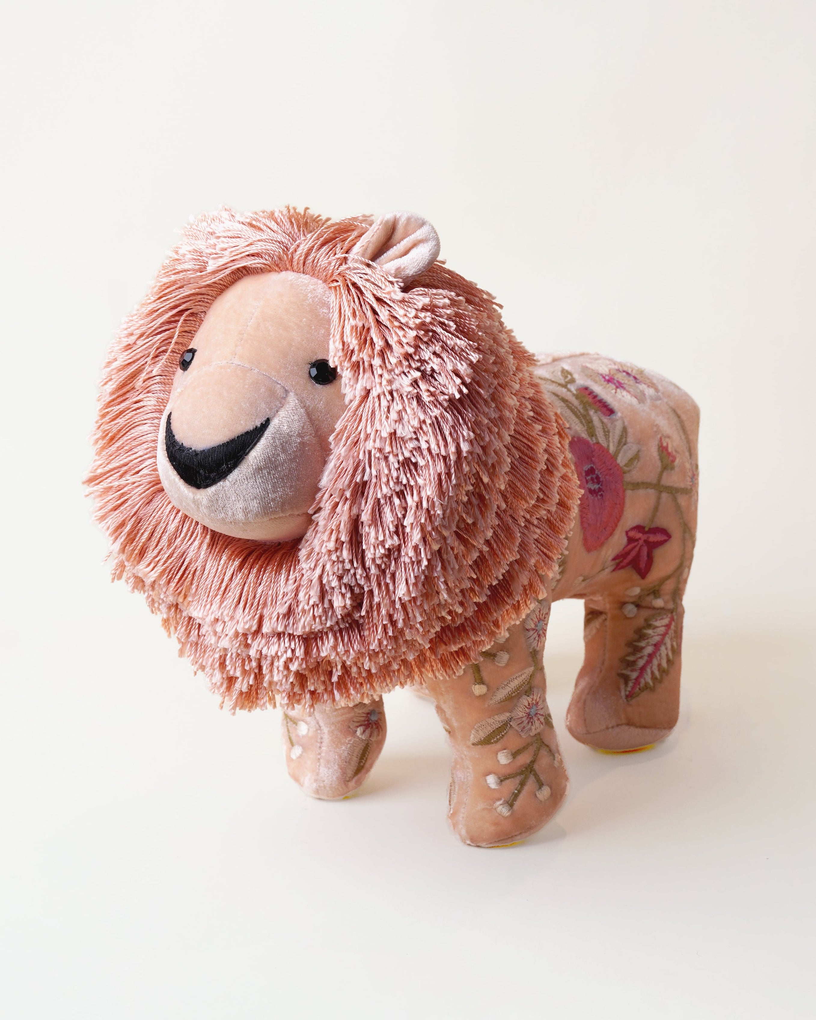 A handmade plush lion toy with a shaggy pink mane and a patterned tan body, photographed on a clean off-white background.