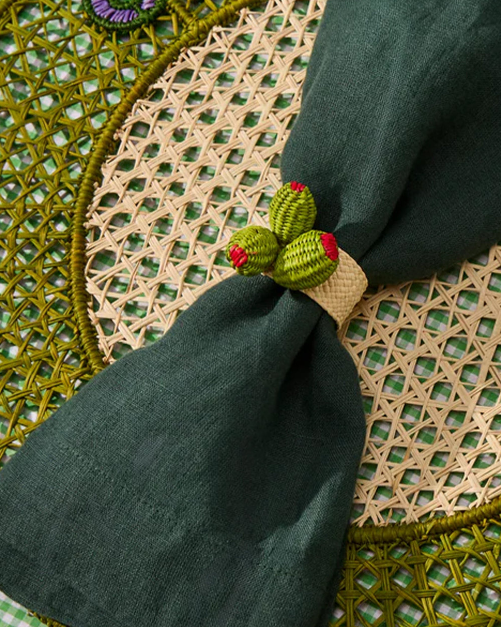 Green napkin folded into a decorative shape on a woven placemat with a checkered tablecloth.
