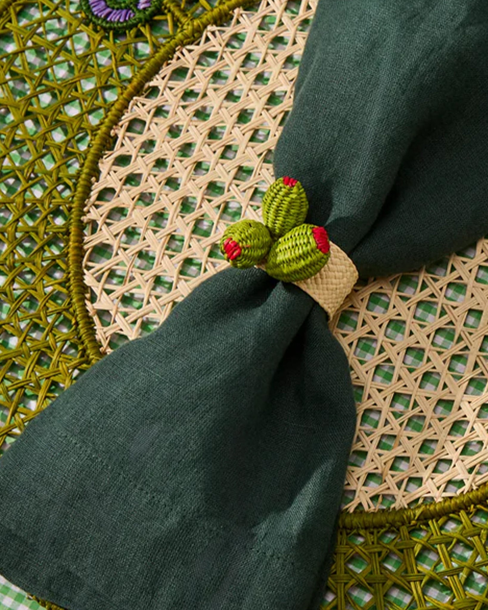 Green napkin folded into a decorative shape on a woven placemat with a checkered tablecloth.