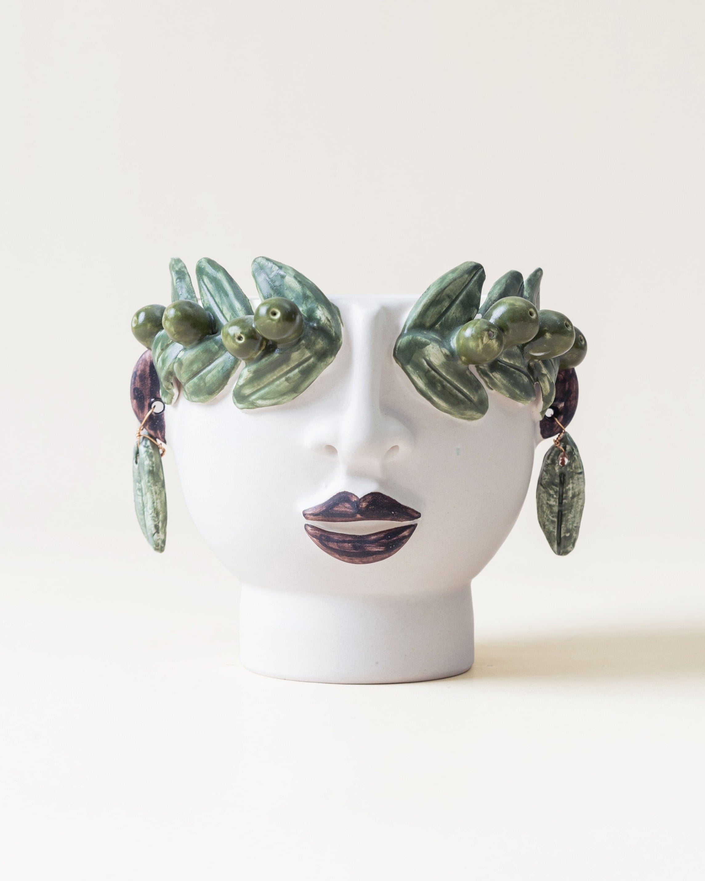 Ceramic face with green leaf-like earrings on a white background