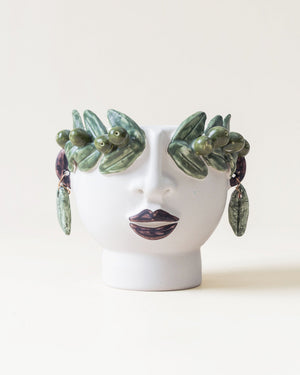 Ceramic face with green leaf-like earrings on a white background