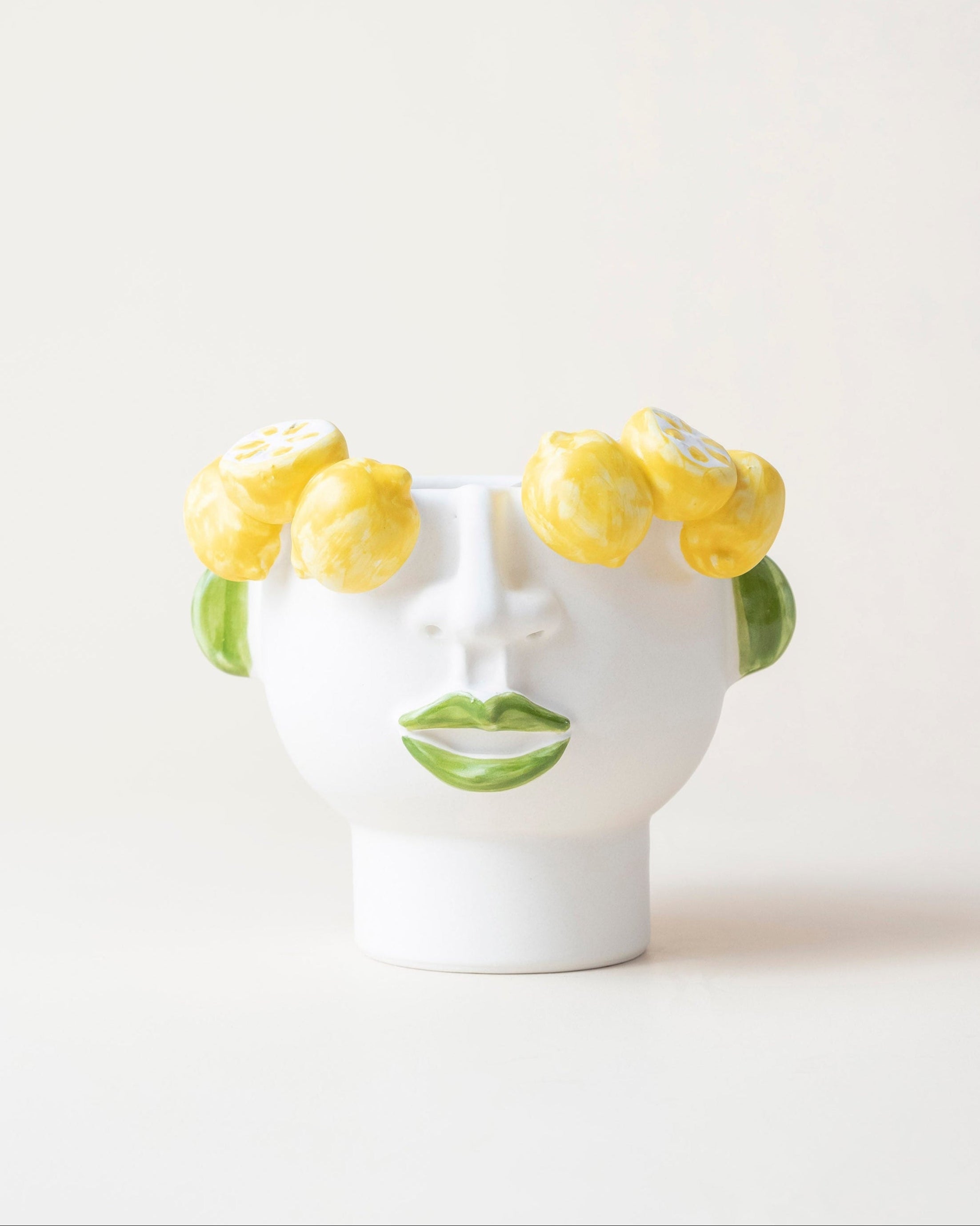 White ceramic vase shaped like a face with yellow flowers on a white background