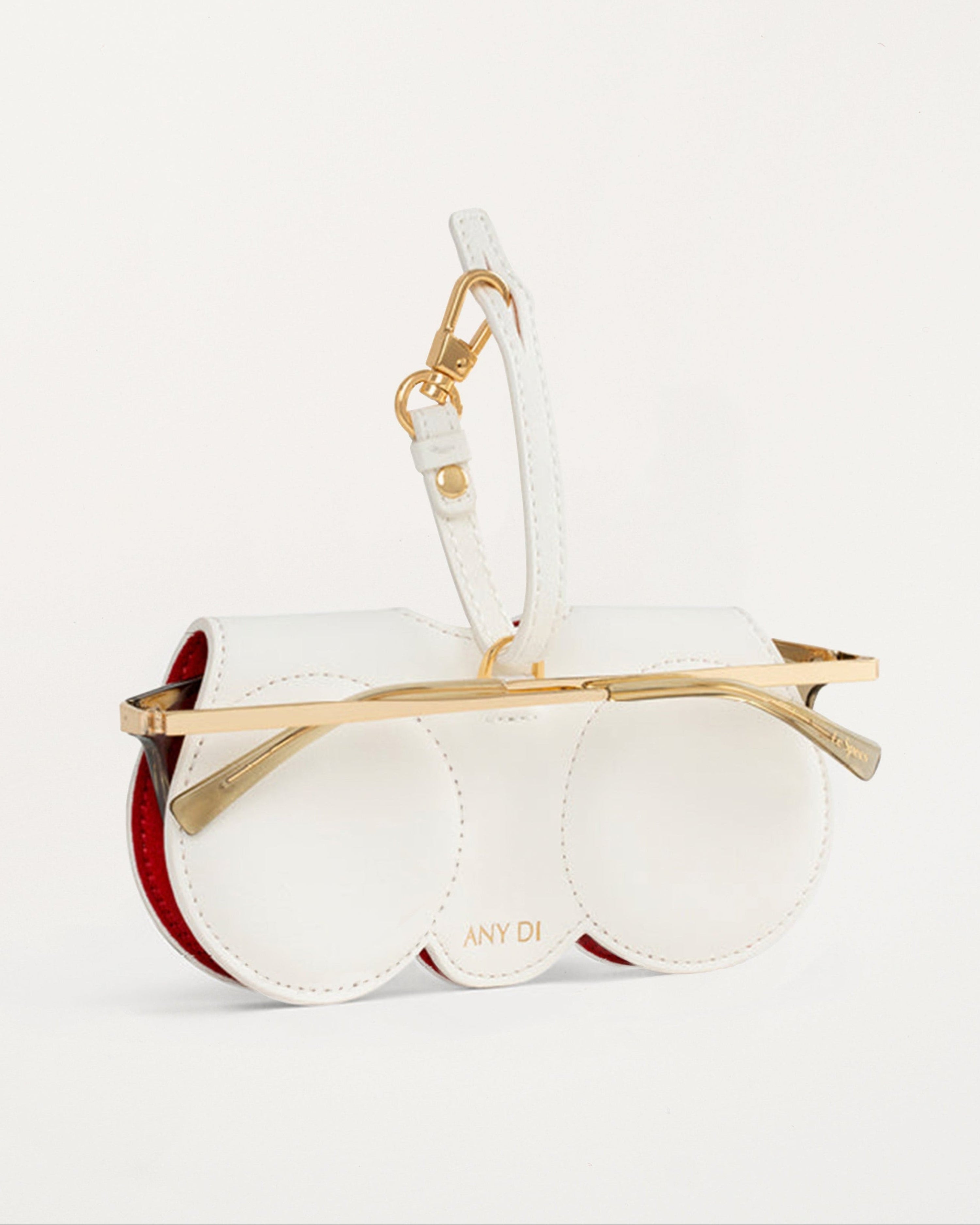 “Diva SunCover sunglasses case in white vegan leather with black round sunglasses face design and glossy red lips, inspired by CEO and designer Anne Dickhardt, gold-plated hardware”

